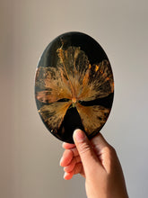 Load image into Gallery viewer, Close-up shot of a dried hibiscus flower embedded in a glossy black resin coaster, featuring detailed petals and a prominently visible pollen stem. The deep black background accentuates the flower’s natural beauty.