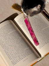 Load image into Gallery viewer, "Unique handmade pink Bougainvillea petal resin bookmark with gold tassel, displayed on an open book for aesthetic appeal.