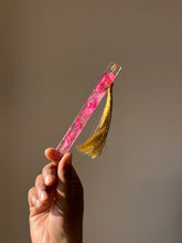 Load image into Gallery viewer, Minimalist pink Bougainvillea petal resin bookmark with a gold tassel, showcased on an open book for book lovers
