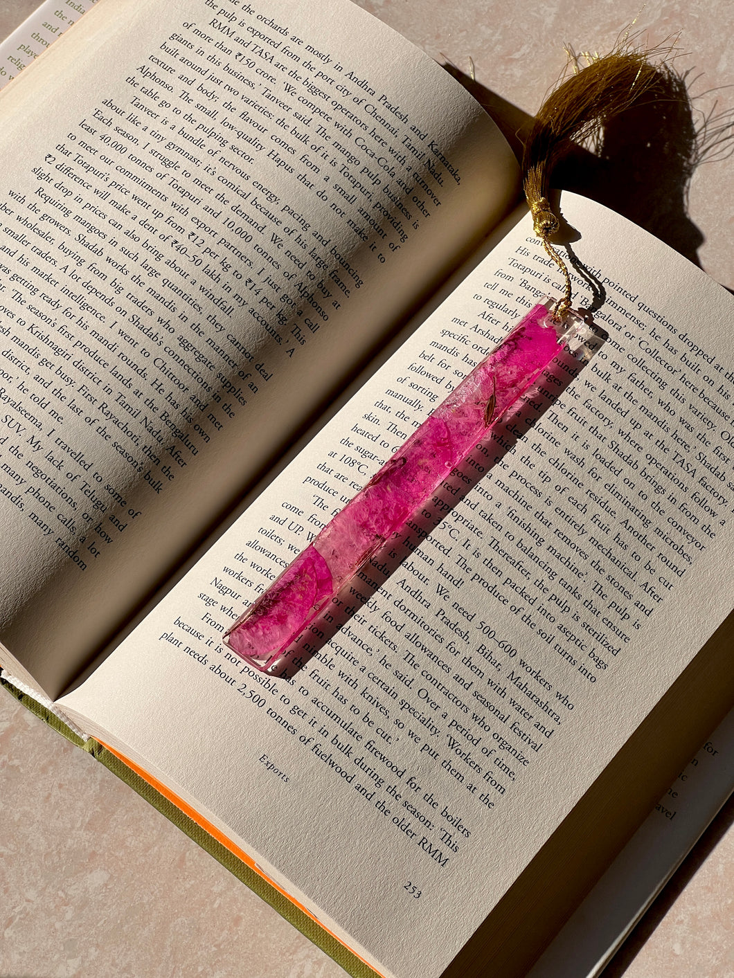 Handmade resin bookmark with pressed pink petals and a gold tassel, placed on an open book for book lovers