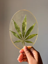 Load image into Gallery viewer, Close-up angle of ShopKuhoo oval resin hemp leaf coaster, highlighting the preserved hemp leaf&#39;s unique texture, encased in clear resin for a one-of-a-kind design.

